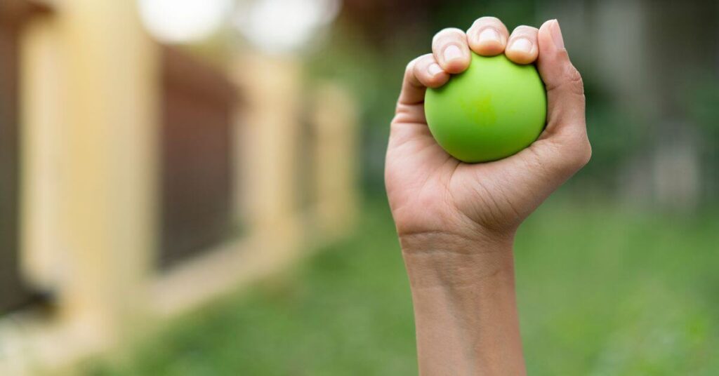 A hand holding a green stress ball outdoors