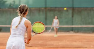 A woman prepares to return a serve during a match on a clay court, showcasing a key moment in Tennis Basics for Beginners with focus on stance and positioning.