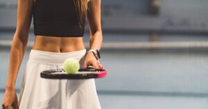 a person balancing a ball on a tennis racket in crop top and white tennis skirt
