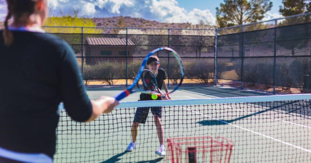 Two players training on a tennis court applying what the tennis coach online taught them