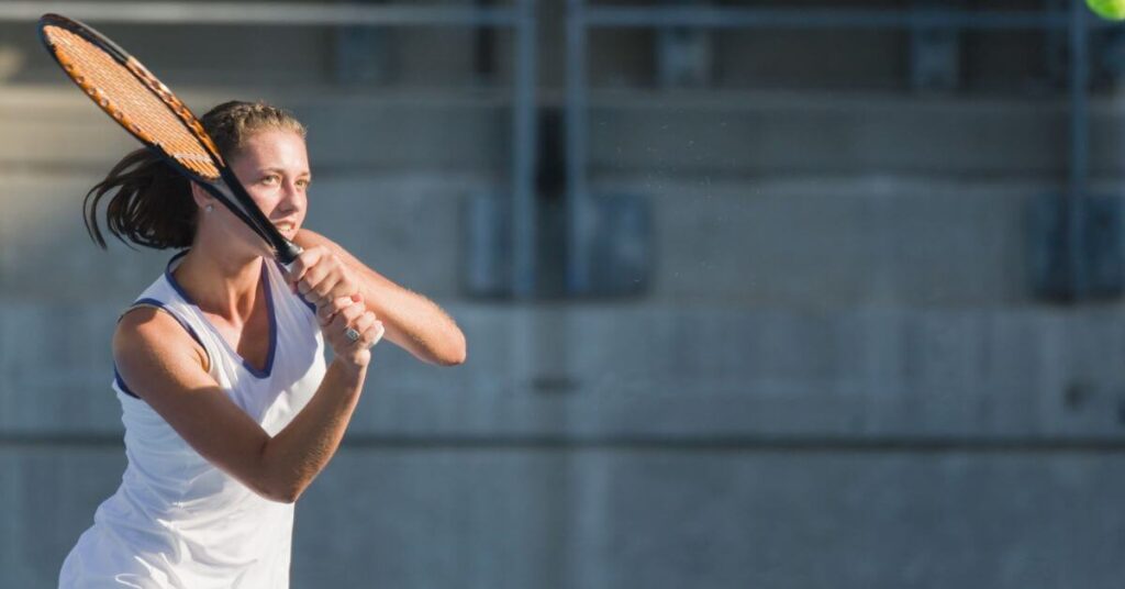A tennis player in a hitting stance on an outdoor court showing a great form, one of the health benefits of tennis