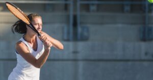 A tennis player in a hitting stance on an outdoor court showing a great form, one of the health benefits of tennis