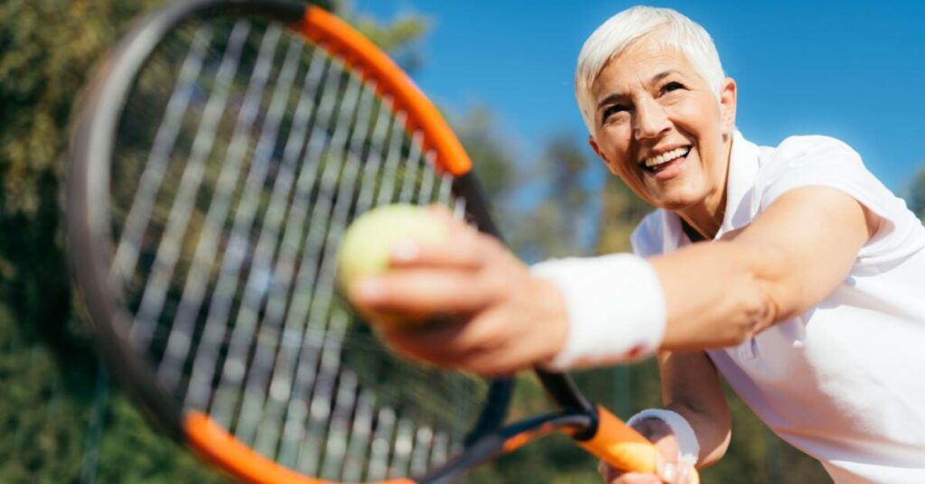 An active elder tennis player smiling while holding the tennis ball on a tennis racket showing the effects of health benefits of tennis