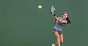 A tennis player swinging to hit the tennis ball with a green background on her way to become one of the famous women tennis players