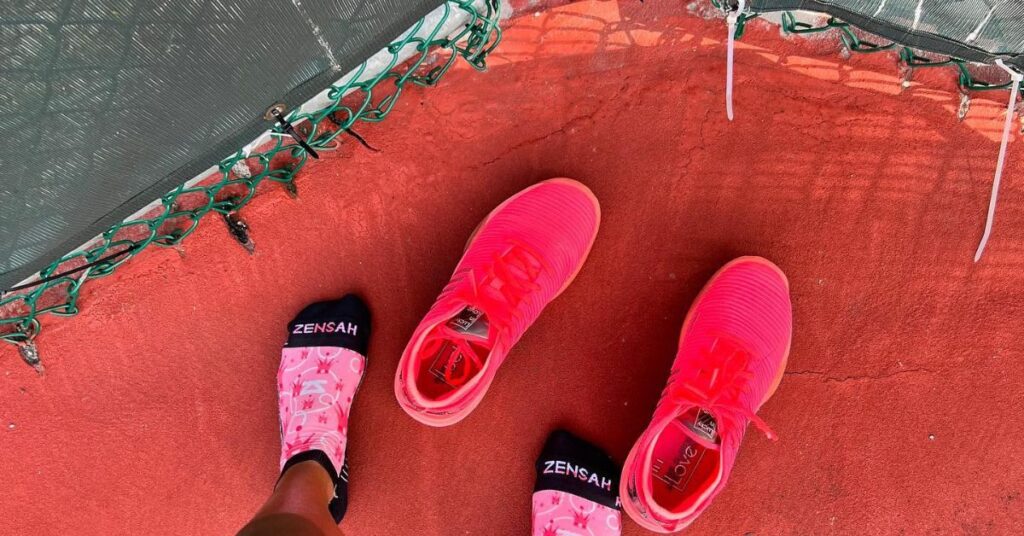 A pair of red neon shoes and feet wearing pink and black socks, one of the best tennis accessories to have