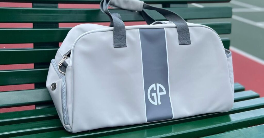 A duffle bag in white and gray colors on a green bench, one of the best tennis coach gifts