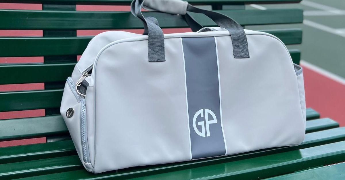A duffle bag in white and gray colors on a green bench, one of the best tennis coach gifts